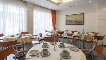 Uma sala de jantar de hotel com mesas redondas, cadeiras e um quadro na parede.