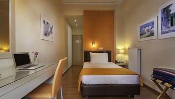 A hotel room with a bed, a desk with a laptop, a chair, and a suitcase.
