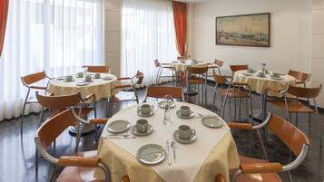 A dining area with round tables, chairs, and neatly set tables with plates, cups, and cutlery.