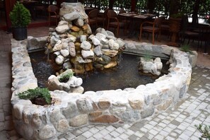 A stone fountain with water cascading down, surrounded by a stone border and potted plants. - Aristocrat Hotel (Skopje)