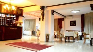 A hotel reception area with a reception desk, a chandelier, a dining area with tables and chairs, and a red carpet. - Aristocrat Hotel (Skopje)