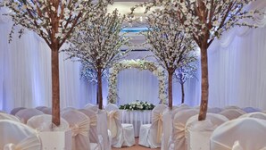 Une allée bordée de chaises blanches et surmontée d’une arche décorée de fleurs.