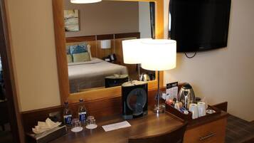 Habitación de hotel con cama, escritorio con cafetera, televisor y espejo.