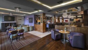 Un hall d’hôtel moderne doté d’un bar, de différents espaces de détente et d’une cheminée.