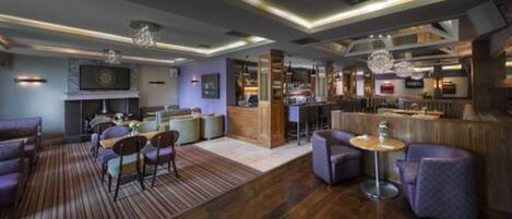 A modern hotel lobby with a bar area, seating arrangements, and a fireplace.