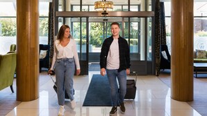 Un hall d’hôtel moderne avec une entrée en verre, des colonnes en bois et un tapis bleu.