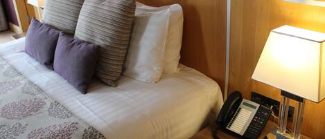 A neatly made bed with a patterned bedspread, a bedside telephone, and a lamp on a wooden nightstand.