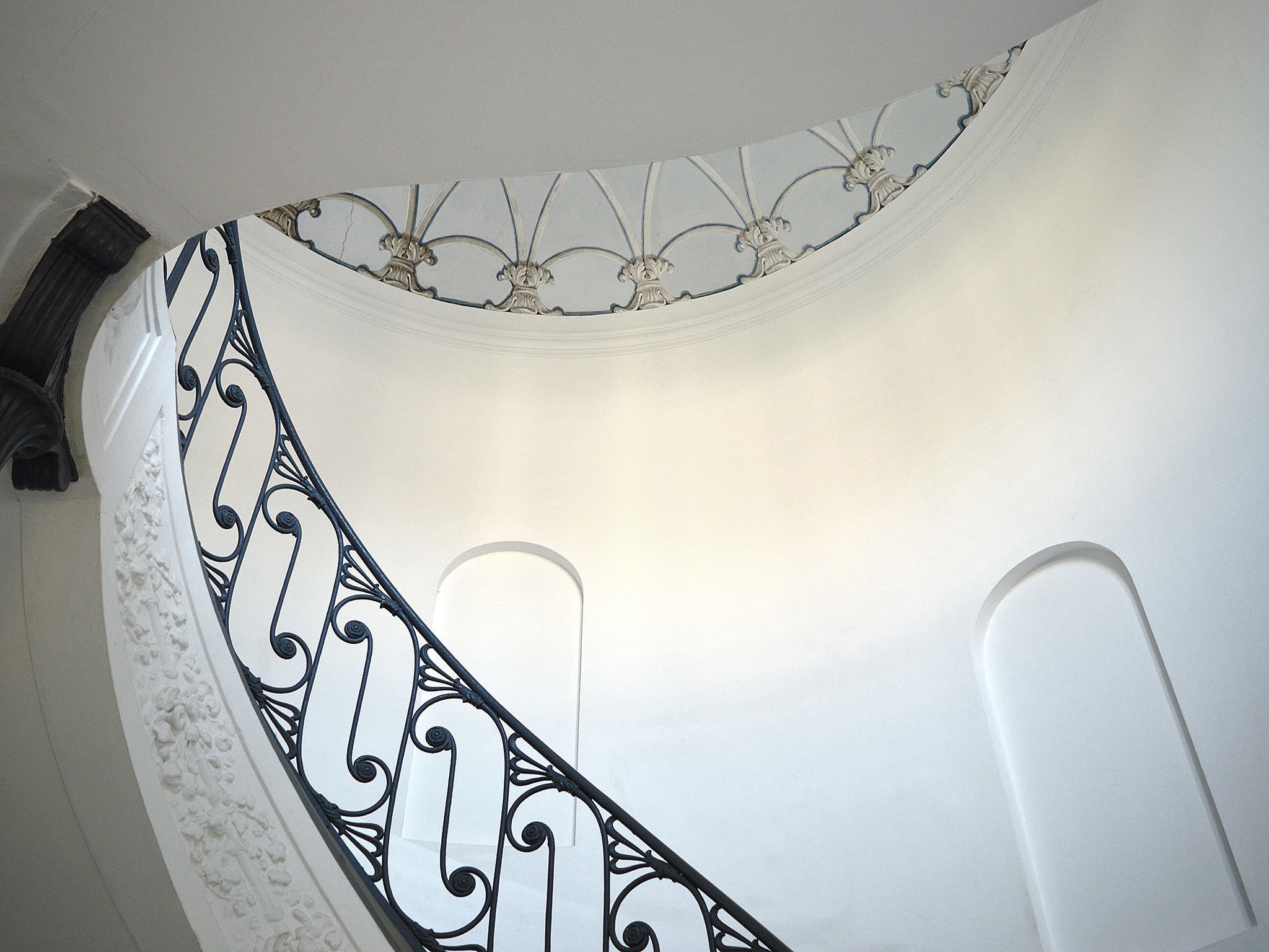 Techo blanco y curvo con elaboradas barandillas de metal negro y molduras decorativas.