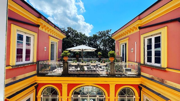 A courtyard with a central open area featuring tables and chairs, surrounded by balconies with railings.