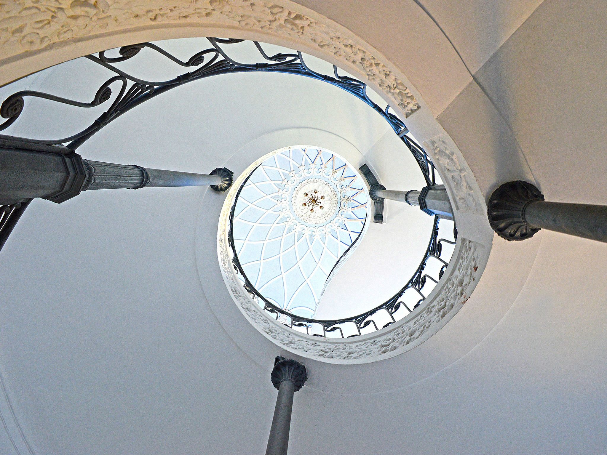 Un escalier en colimaçon surmonté d’un dôme blanc et agrémenté de rampes en métal aux motifs complexes.