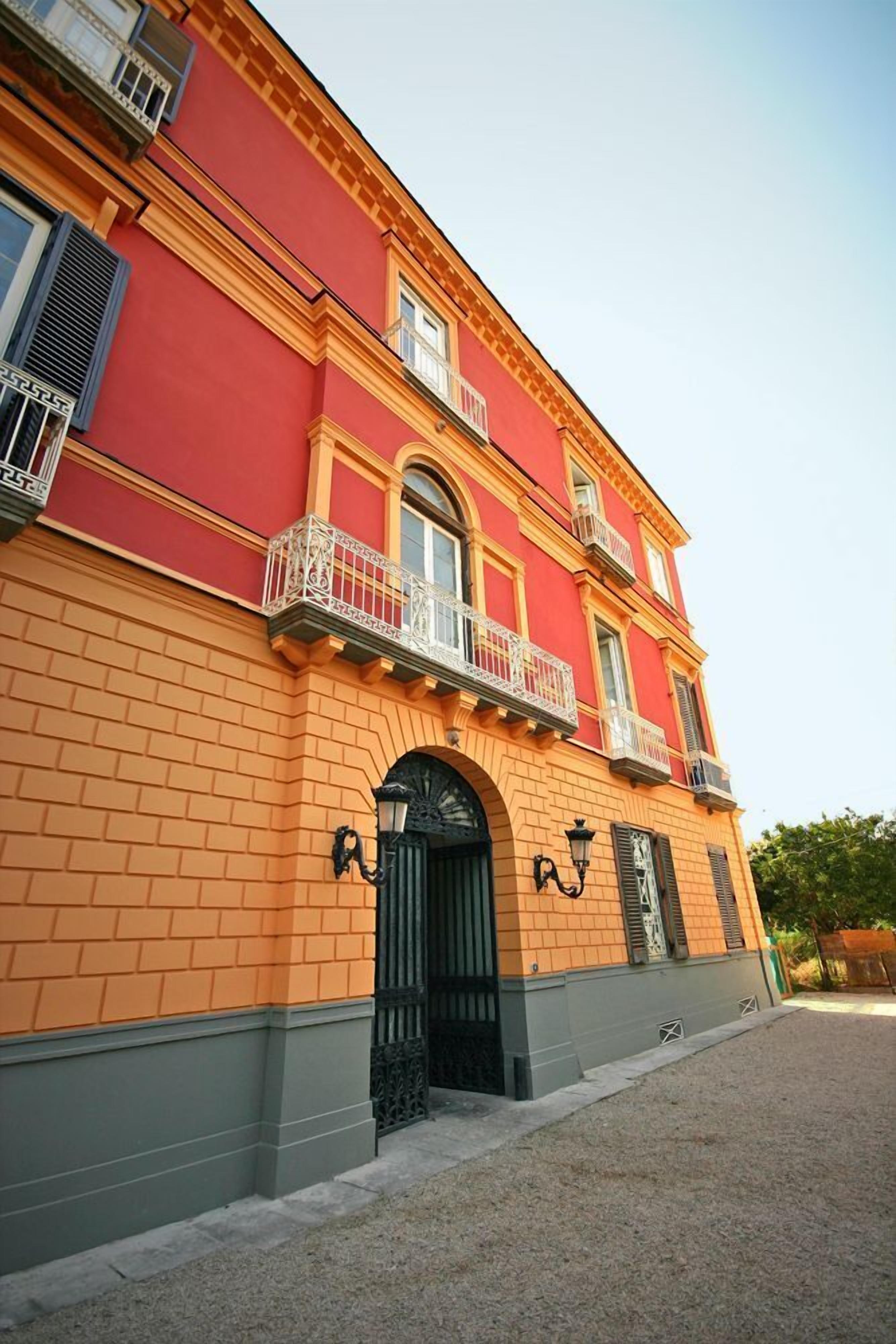 A red and orange building with a black entrance door and white balconies.