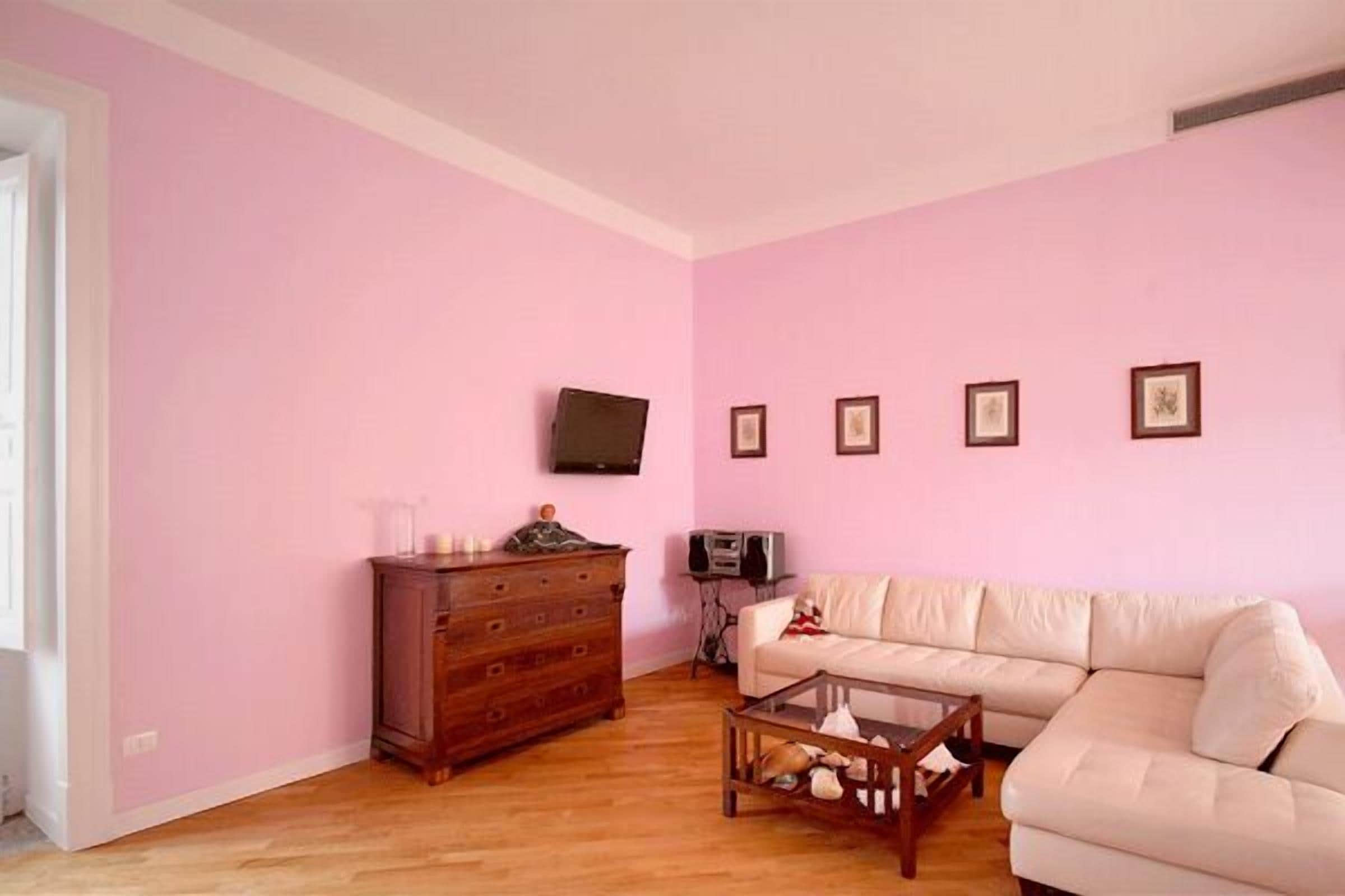 Ett vardagsrum med rosa väggar, en byrå i trä, en beige soffa och ett soffbord.