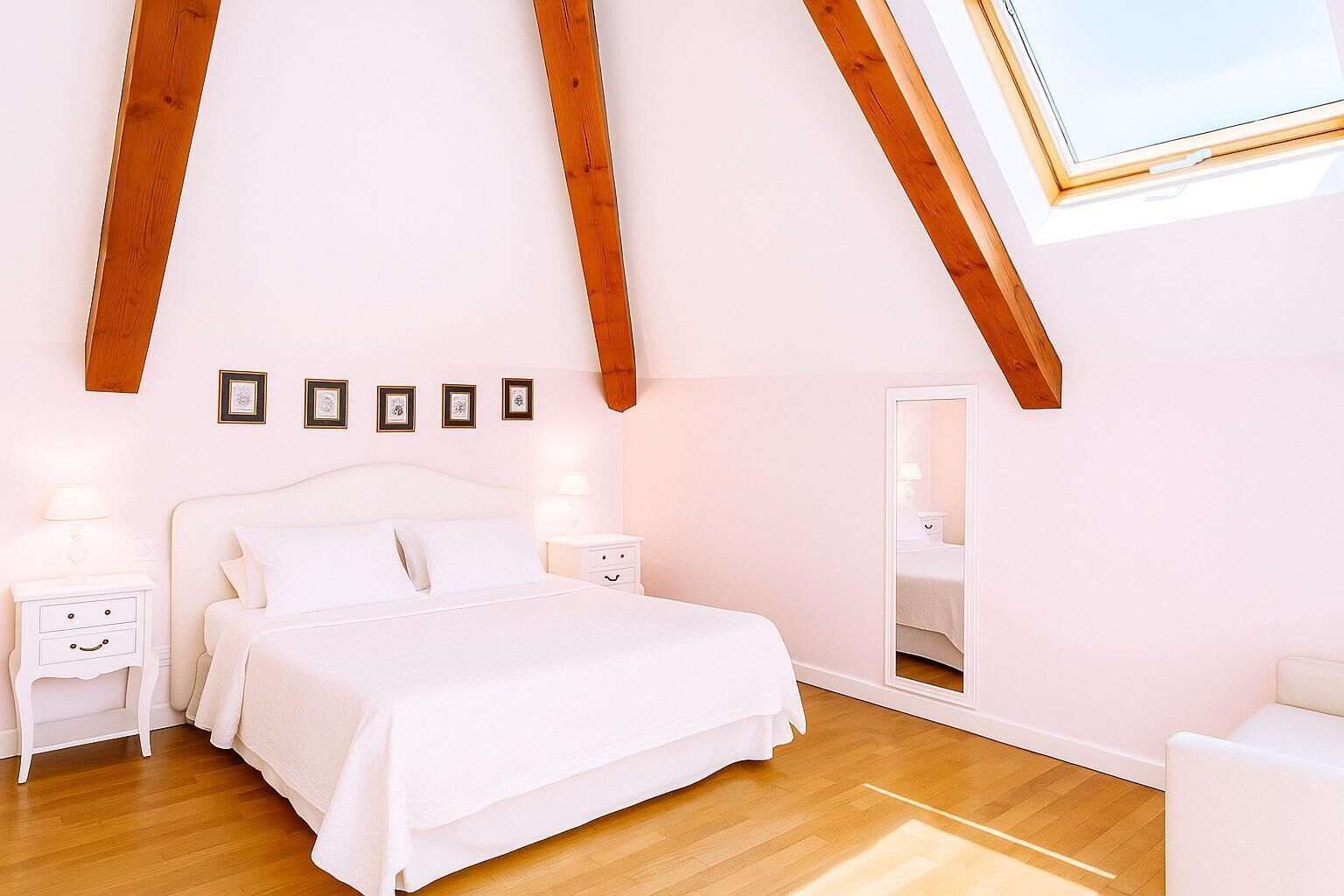 A bedroom with a large bed, wooden beams, a skylight, framed pictures, and a mirror.