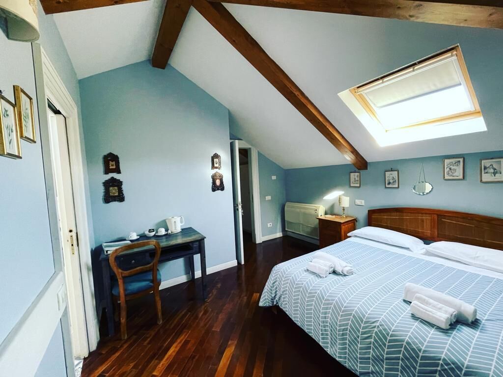 Une chambre à coucher avec un lit, un bureau et une chaise. Il y a une lucarne au-dessus du lit et une porte qui donne sur une autre pièce.