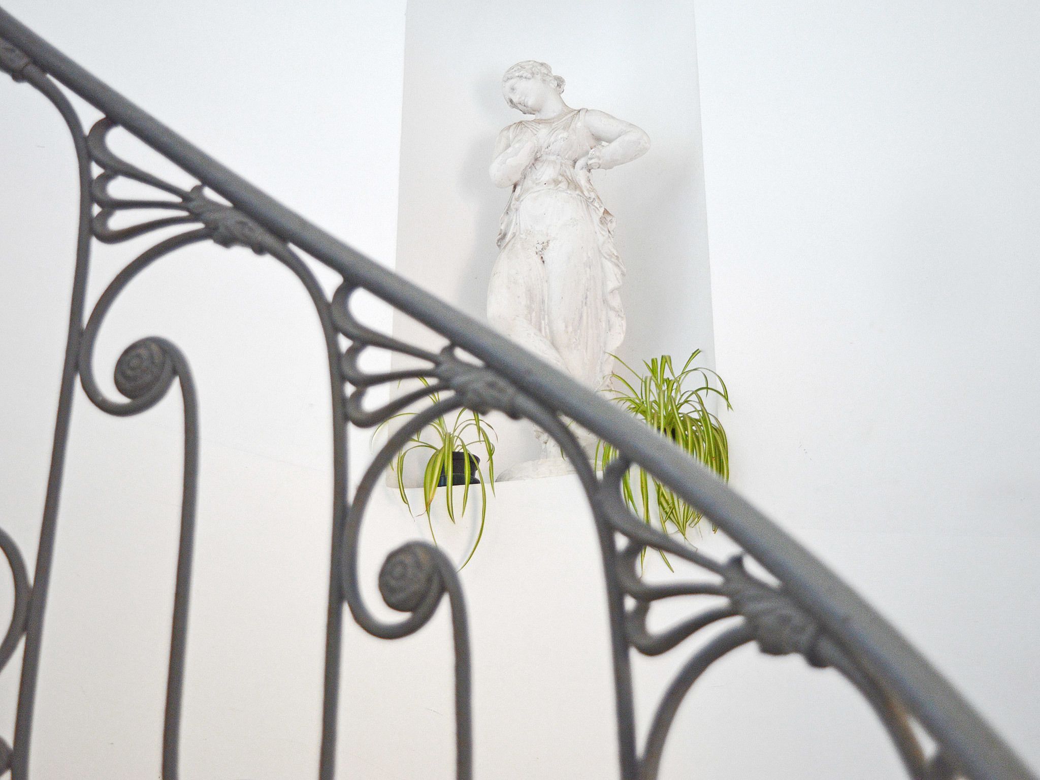 A staircase with a metal railing, a white wall, and a statue.