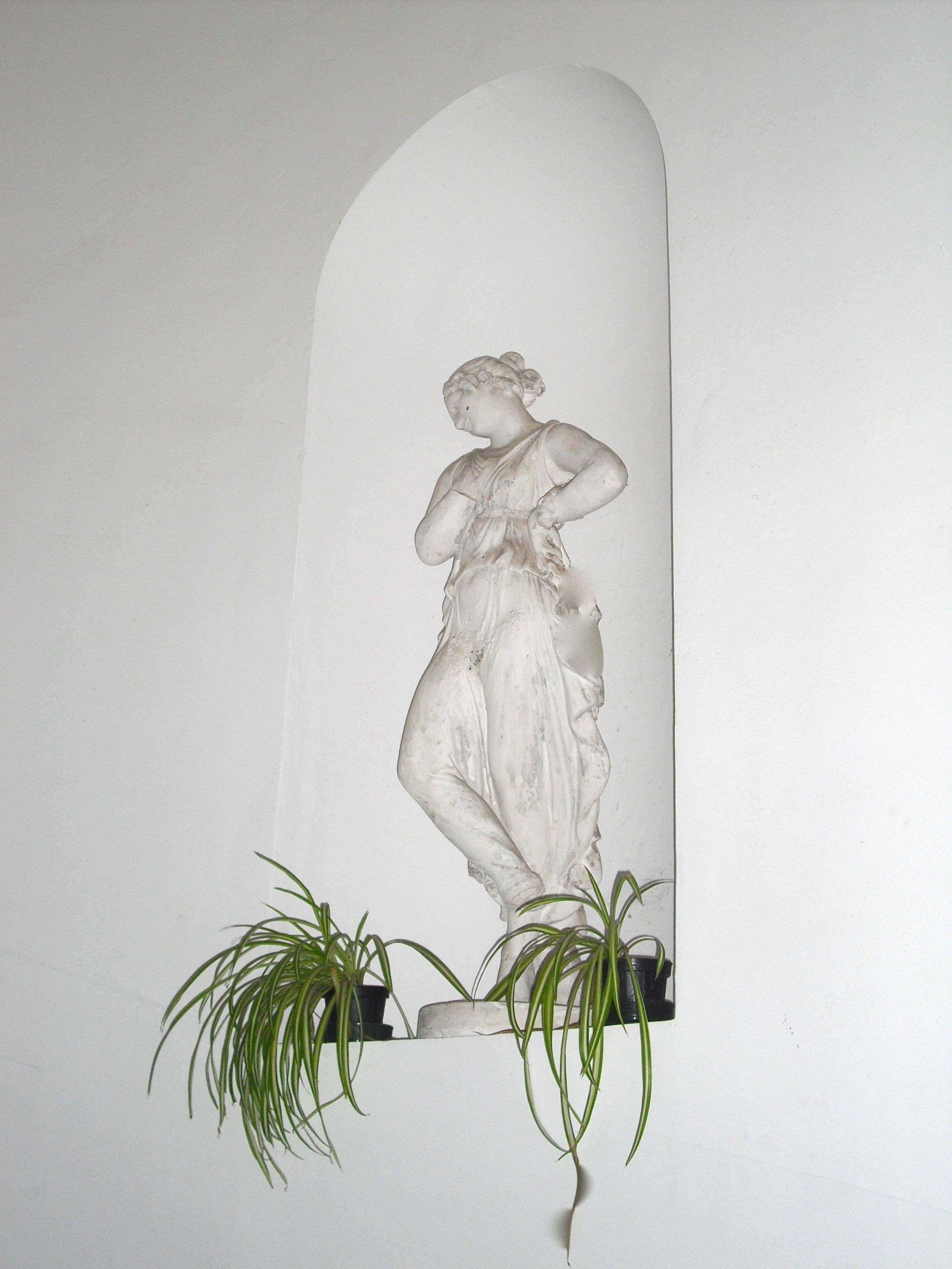 Eine Marmorstatue einer Frau mit einer Pflanze am Fuß.