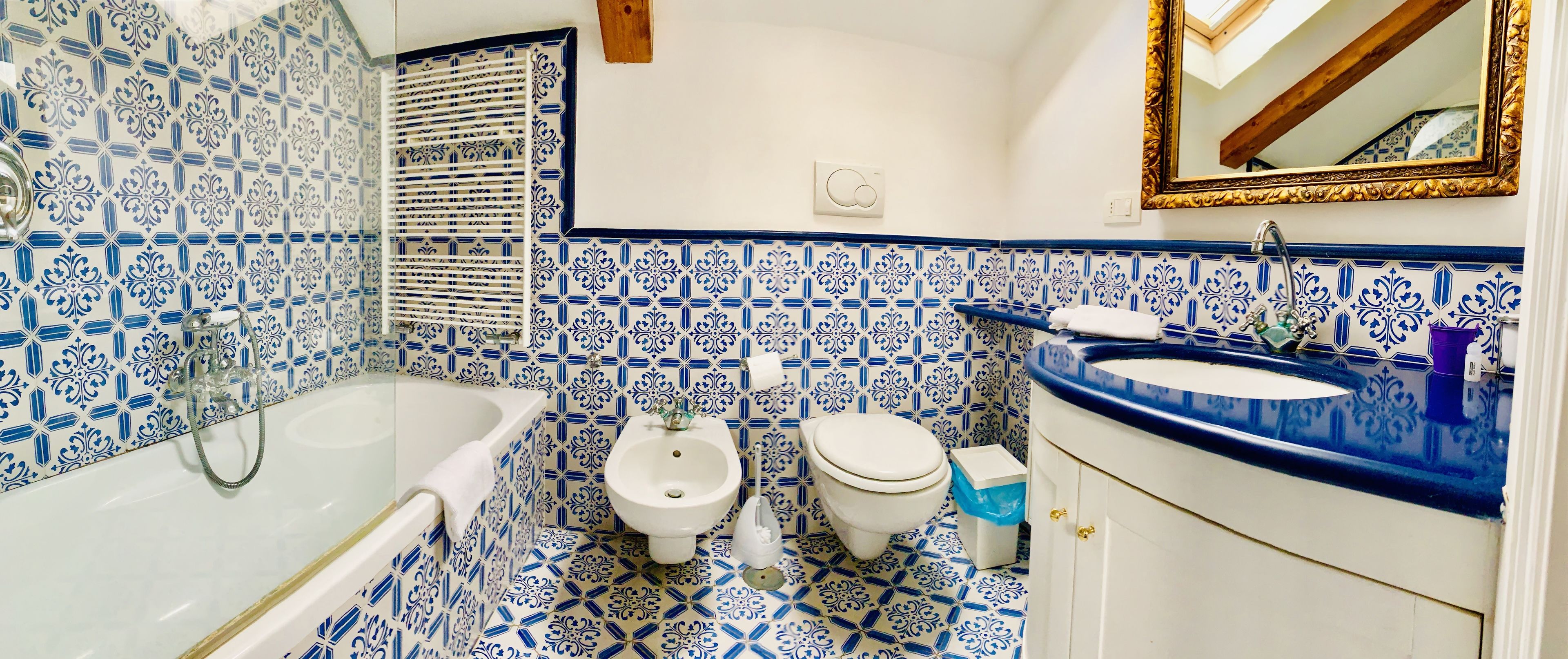A bathroom with blue and white patterned tiles, a bathtub, a sink, a toilet, and a mirror.