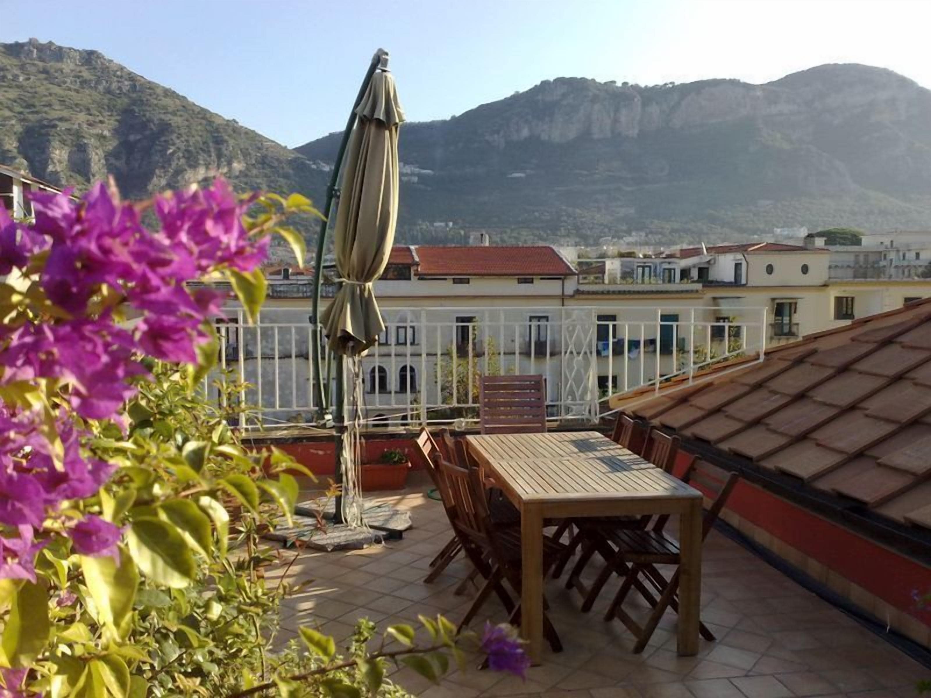 Une terrasse sur le toit, avec une table et des chaises, un parasol, et une vue sur les bâtiments et les montagnes en arrière-plan.