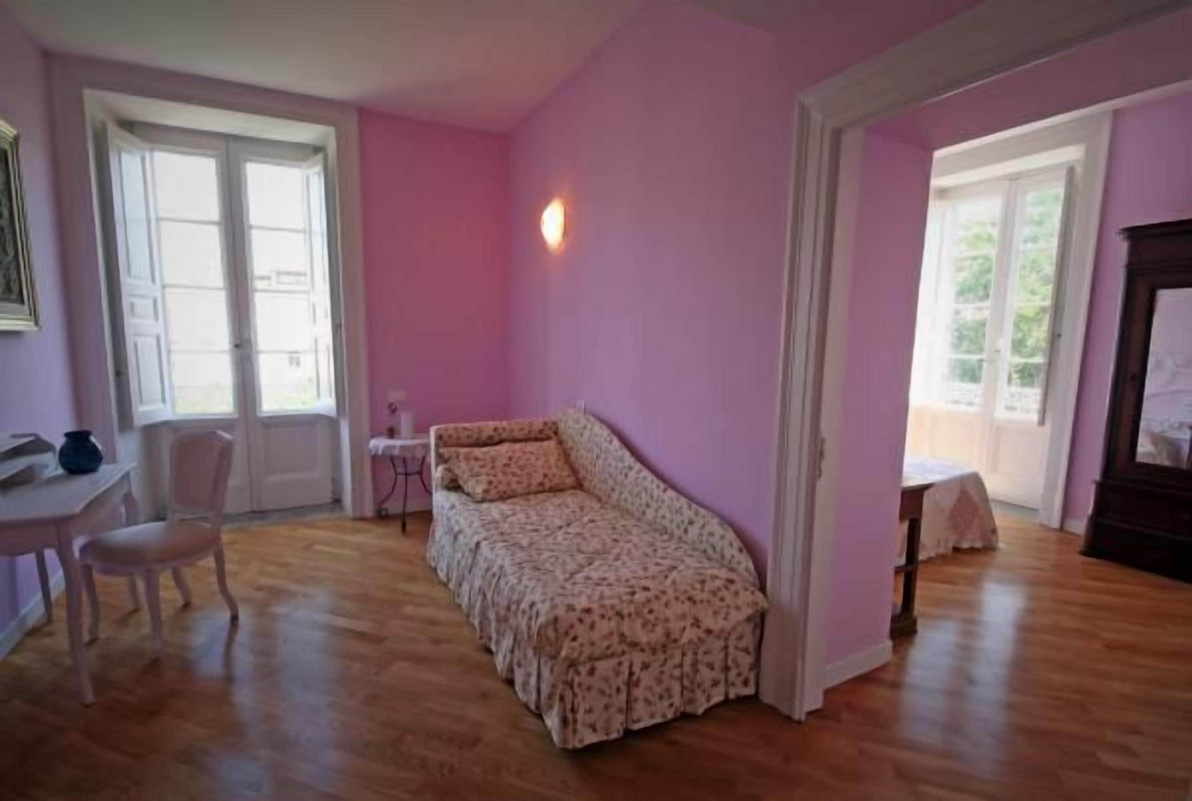 A room with a floral-patterned sofa, a wooden floor, and a pink wall.