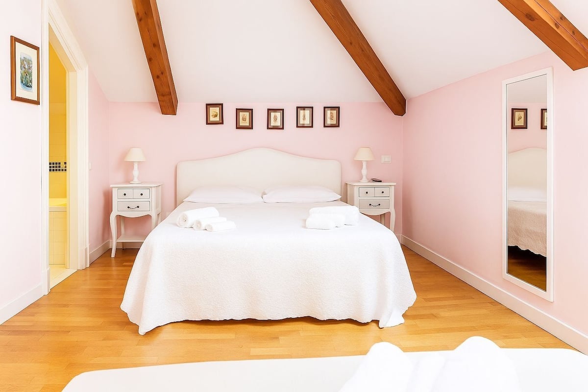 Een slaapkamer met een groot bed, twee nachtkastjes, een spiegel en een houten plafond.