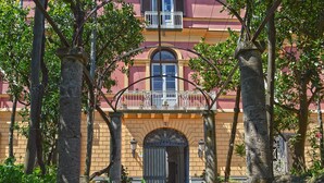 A building with a red entrance, a balcony with white railings, and a door with an arched top.