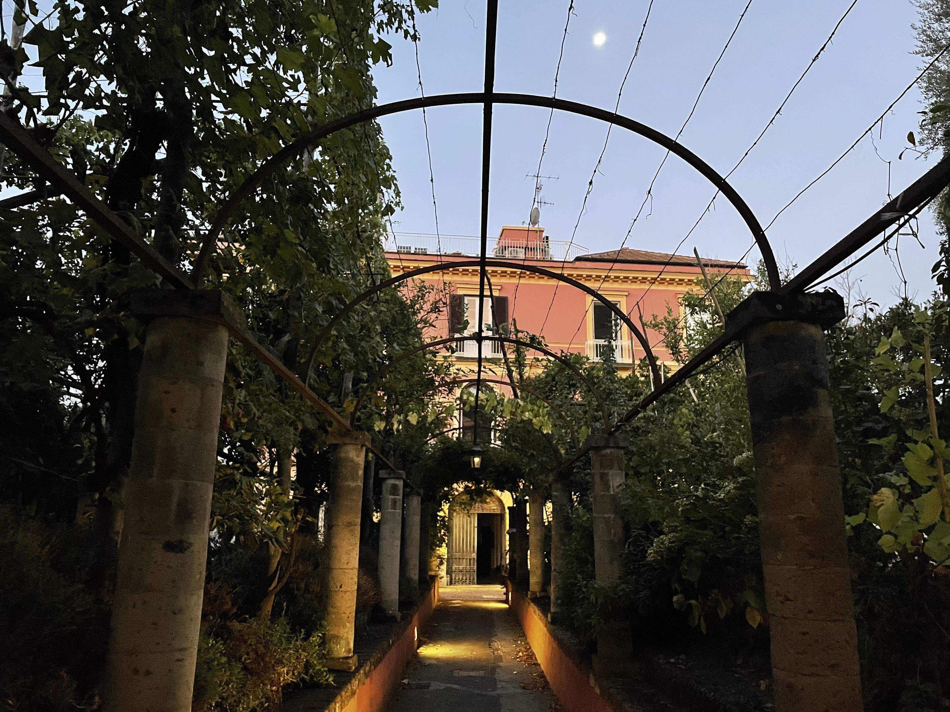 Un sendero con arcos, rodeado de vegetación, que lleva a un edificio de fachada roja.