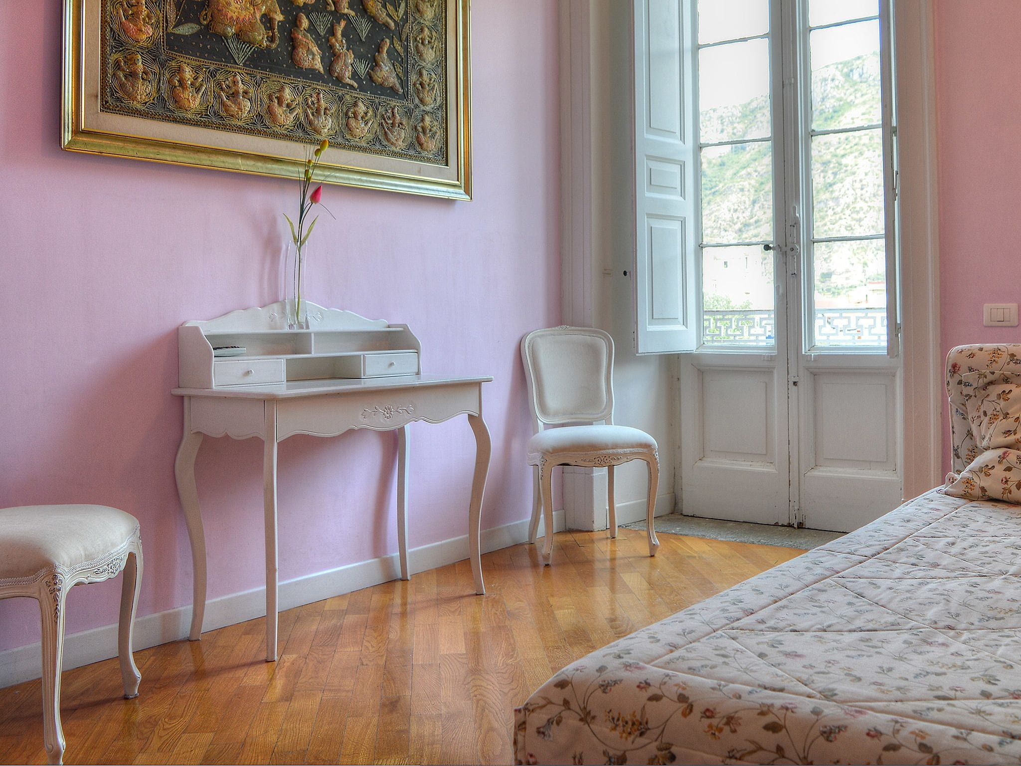 Una habitación con una cama, un escritorio y una silla. Se ve follaje verde por la ventana.