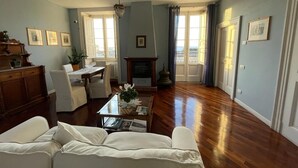 A spacious living room with a wooden floor, a white sofa, a dining table, and a fireplace.