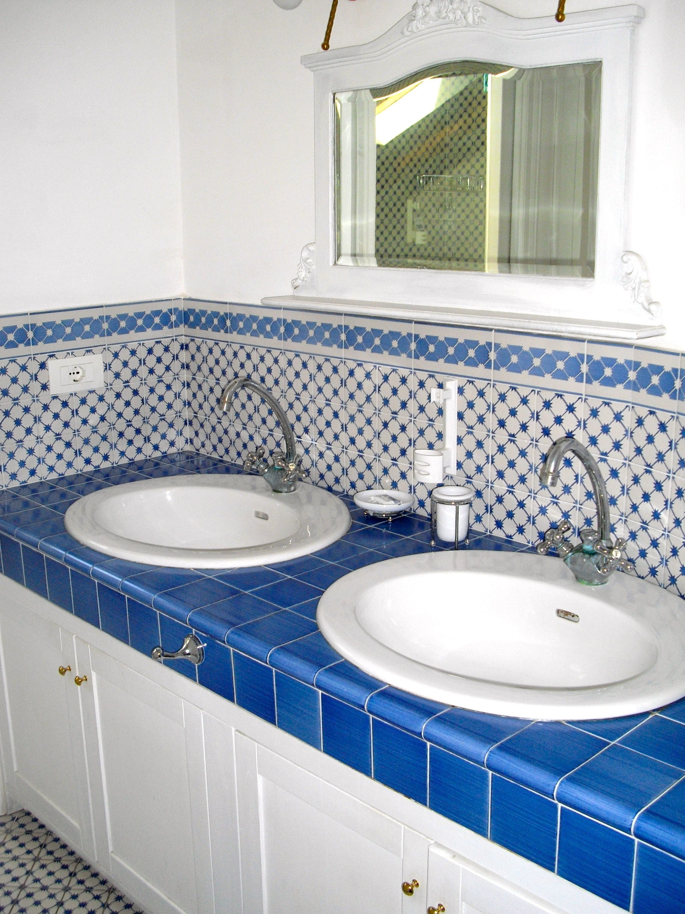 Une salle de bain avec deux lavabos, des carreaux bleus et blancs, et un miroir au-dessus.
