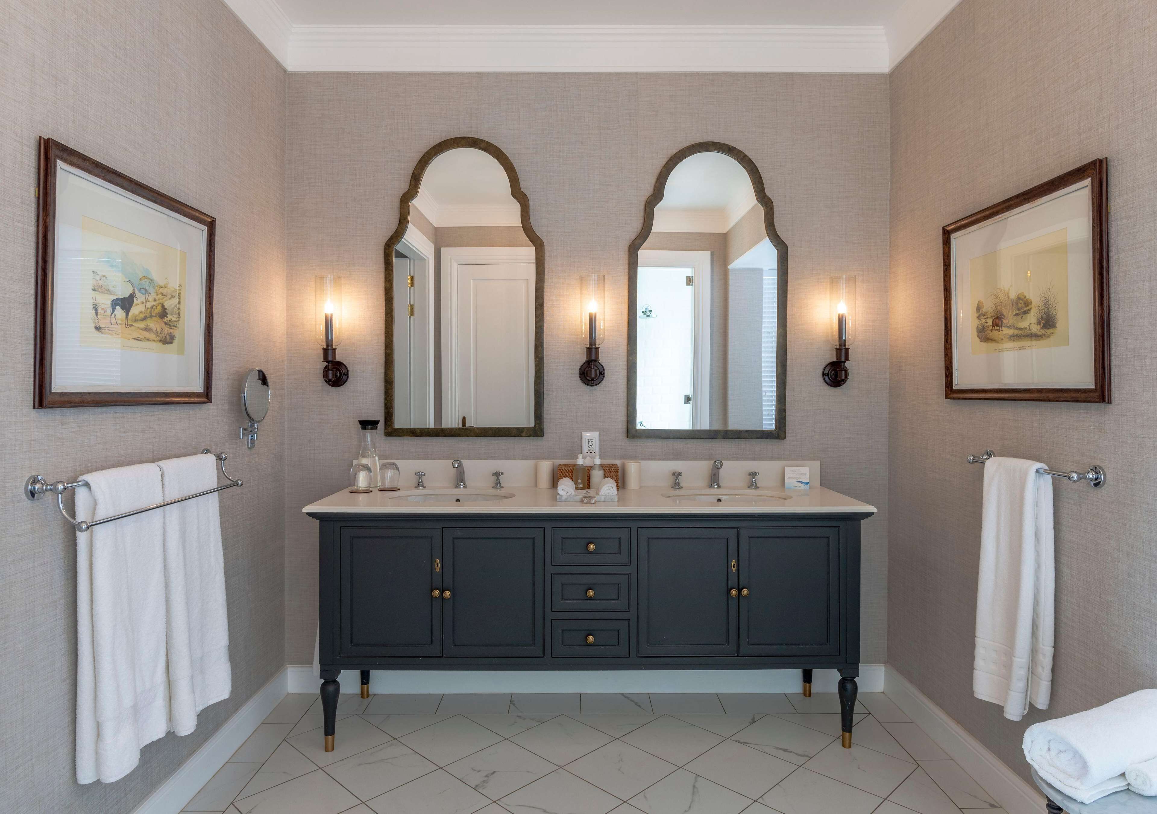 Une salle de bain avec un meuble-lavabo en bois foncé, deux miroirs et des œuvres d’art encadrées accrochées aux murs.