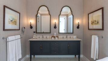 Une salle de bain avec un meuble-lavabo en bois foncé, deux miroirs et des œuvres d’art encadrées accrochées aux murs.