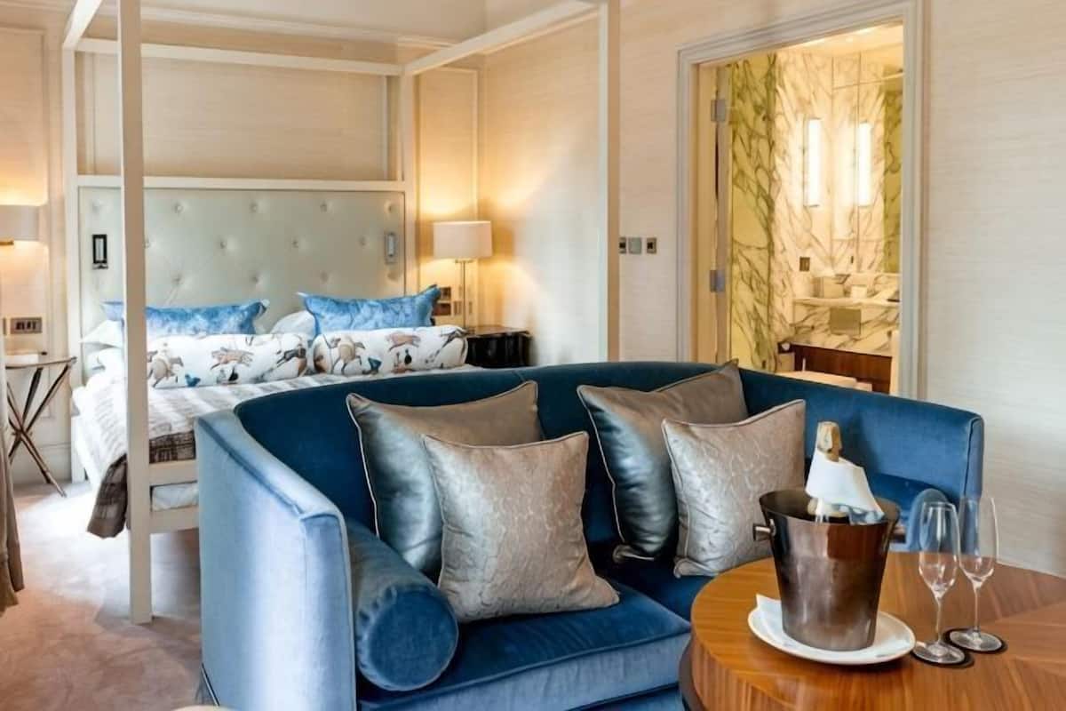 A hotel room with a bed, a blue sofa, a wooden side table, and a marble wall.