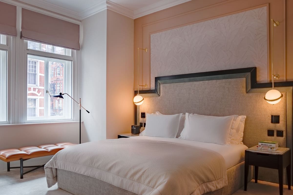 A neatly arranged bedroom with a large bed, bedside tables, a bench, and a view of the outside through a window.