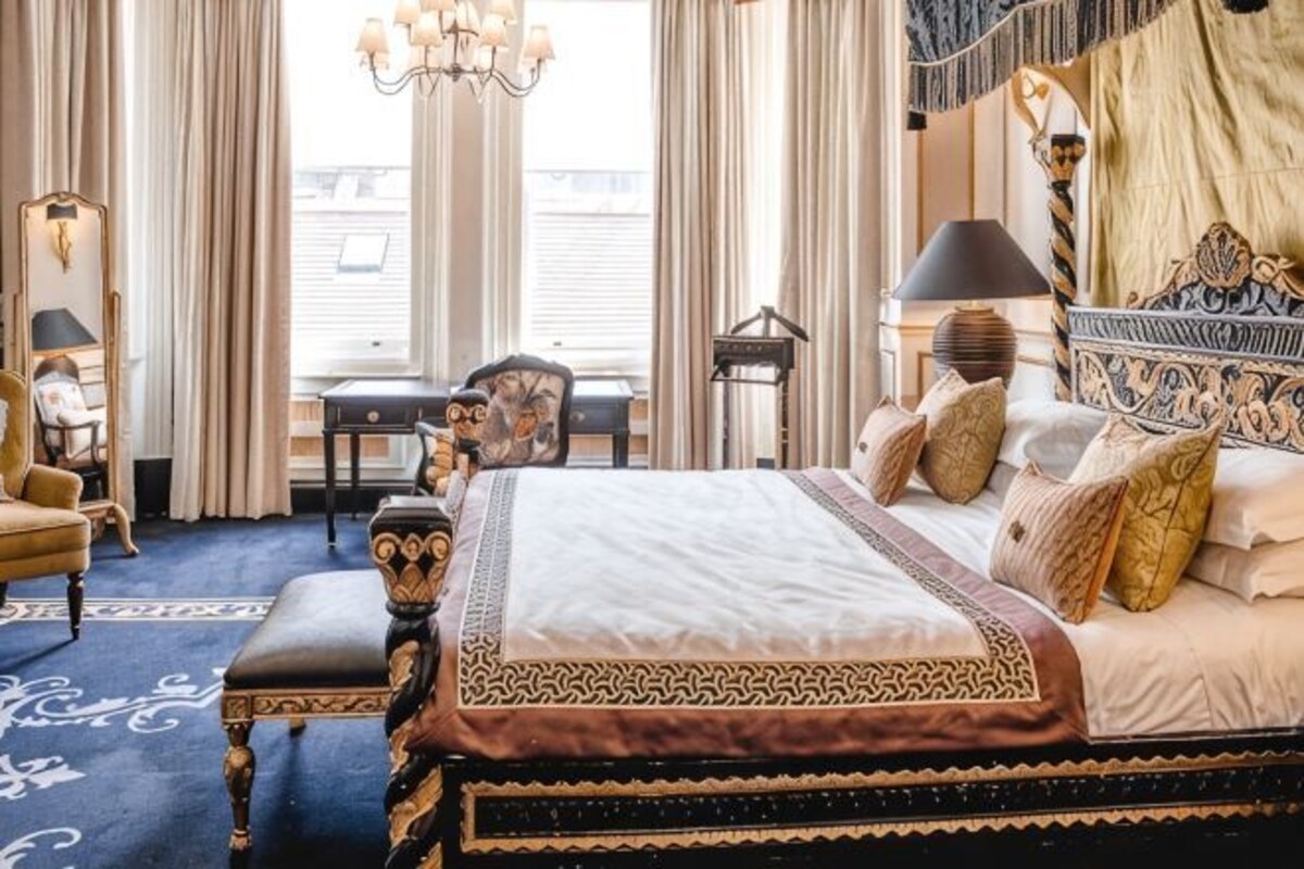 A bedroom with a large bed, a desk, a chair, and a chandelier.