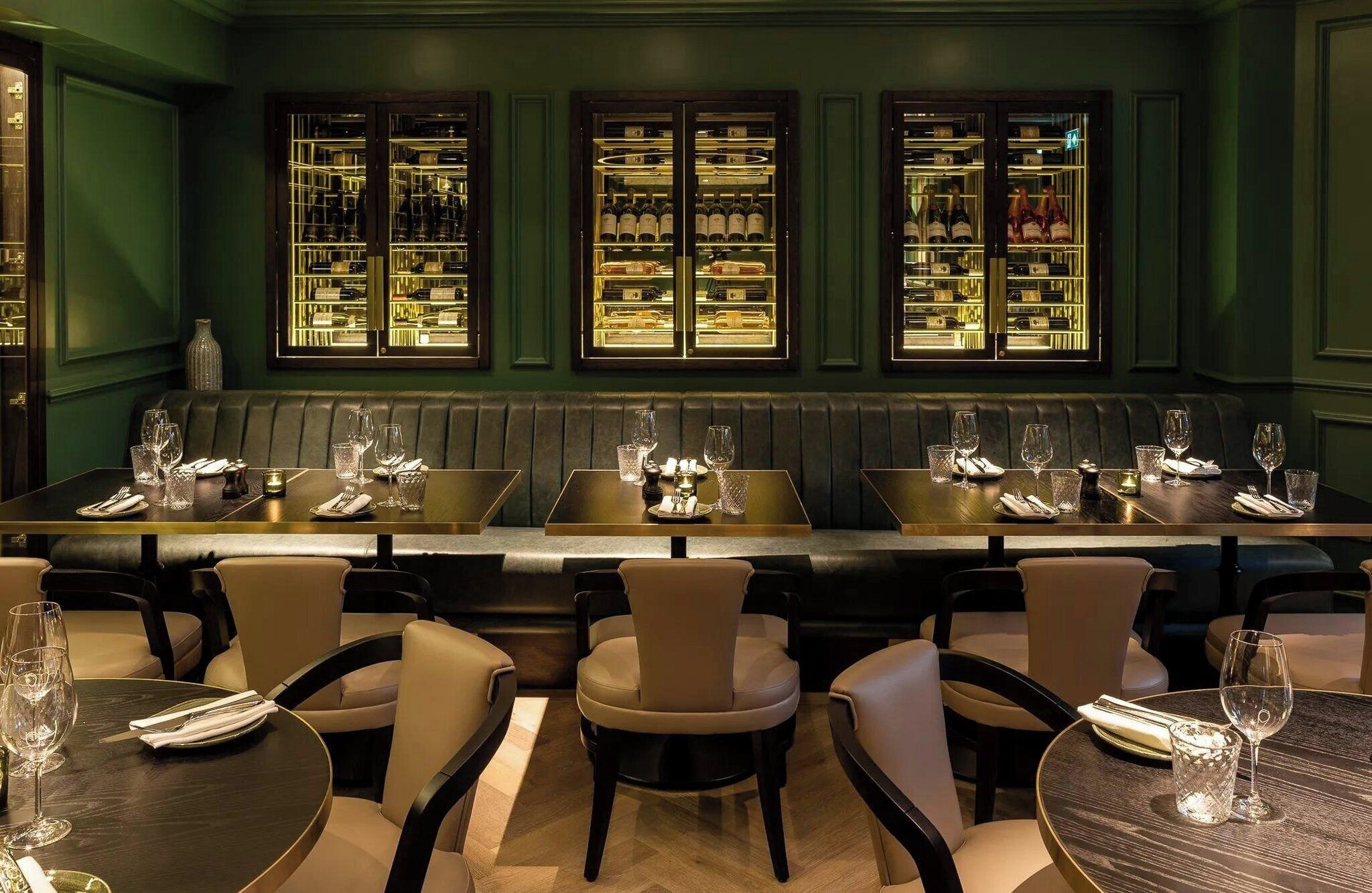 L’intérieur d’un restaurant présente un long banc servant de siège, des tables avec des chaises, et, au fond, un présentoir à vin.