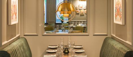 A dining area with a table set for four, a large window with a view of the interior, and a modern pendant light above the table.