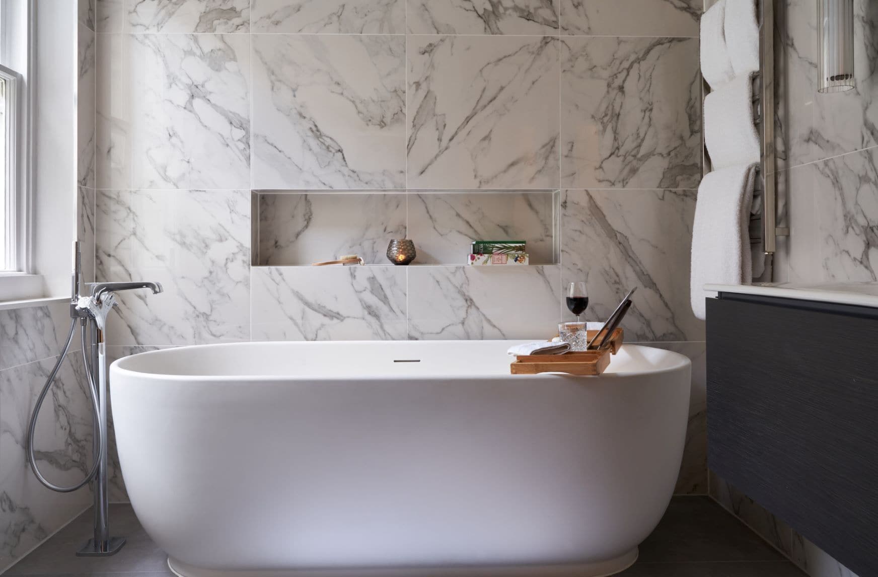 A modern bathroom with a freestanding bathtub, marble walls, and a glass shower enclosure.