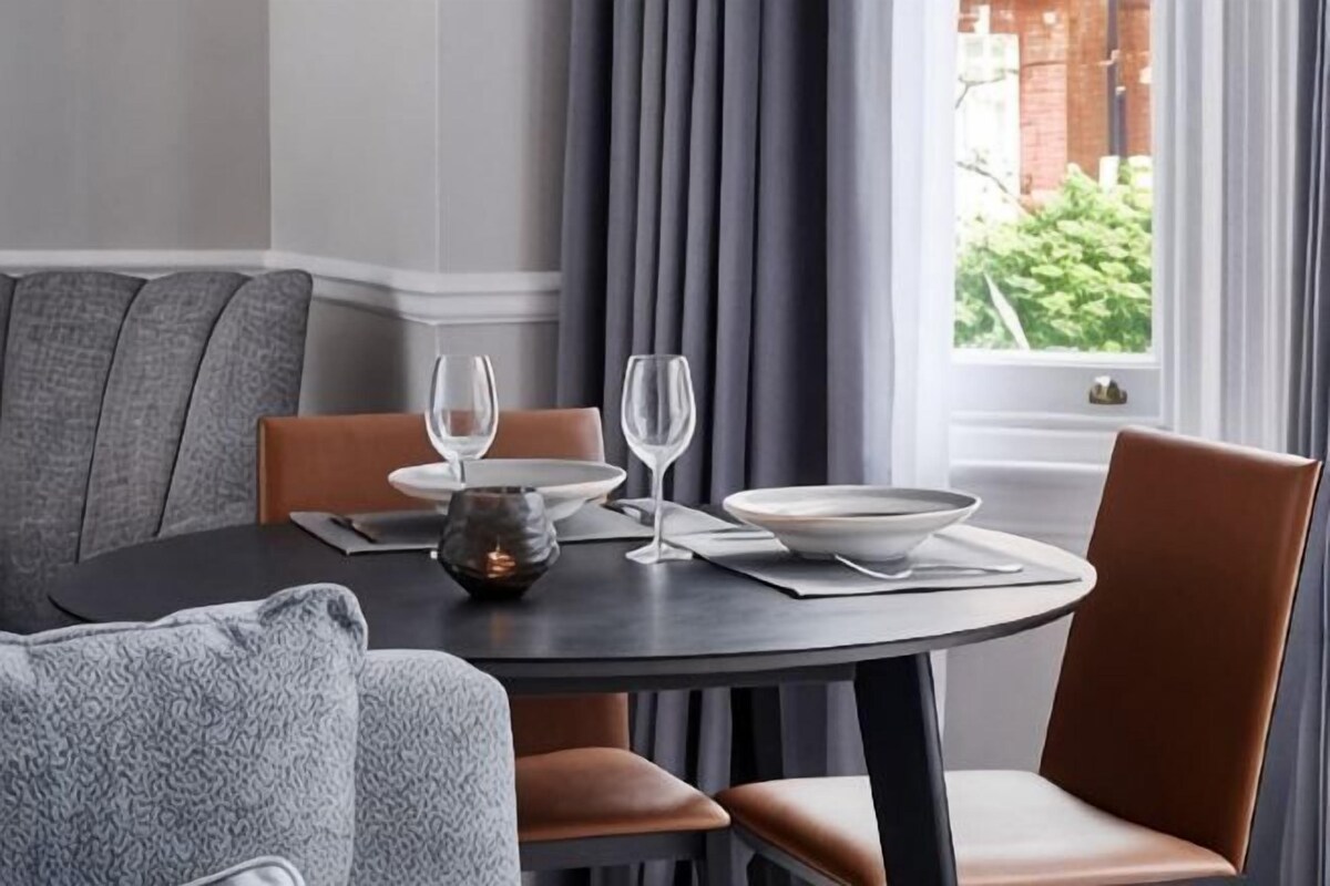 A dining area with a round table, chairs, and a window with curtains.