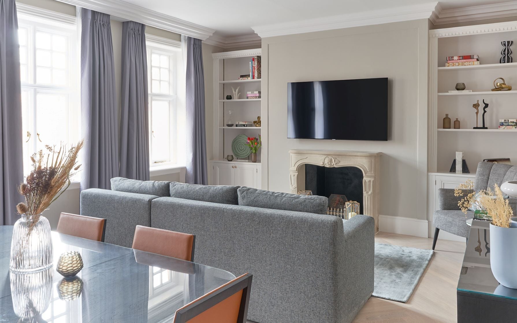 A modern living room with a grey sofa, a fireplace, a flat-screen TV, and a bookshelf.