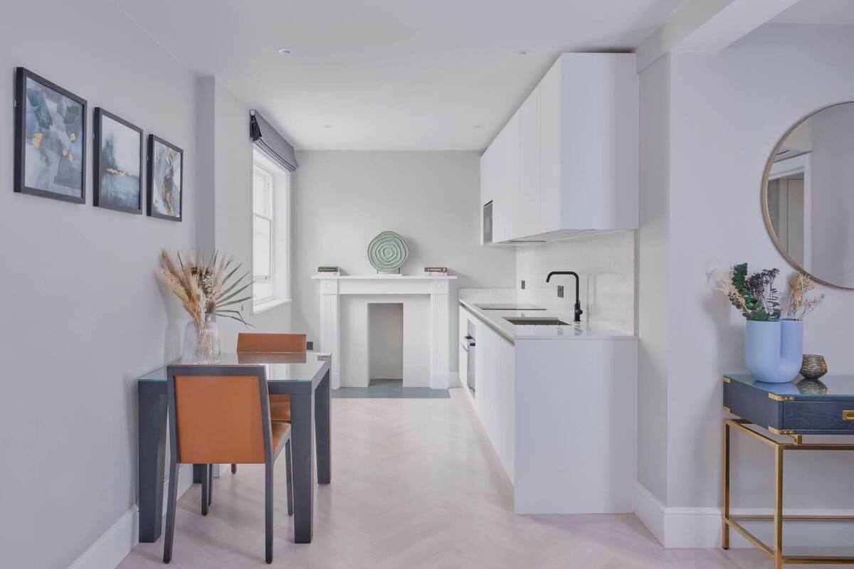 A modern kitchen with white cabinetry, a dining area with a table and chairs, and a small side table with decorative items.