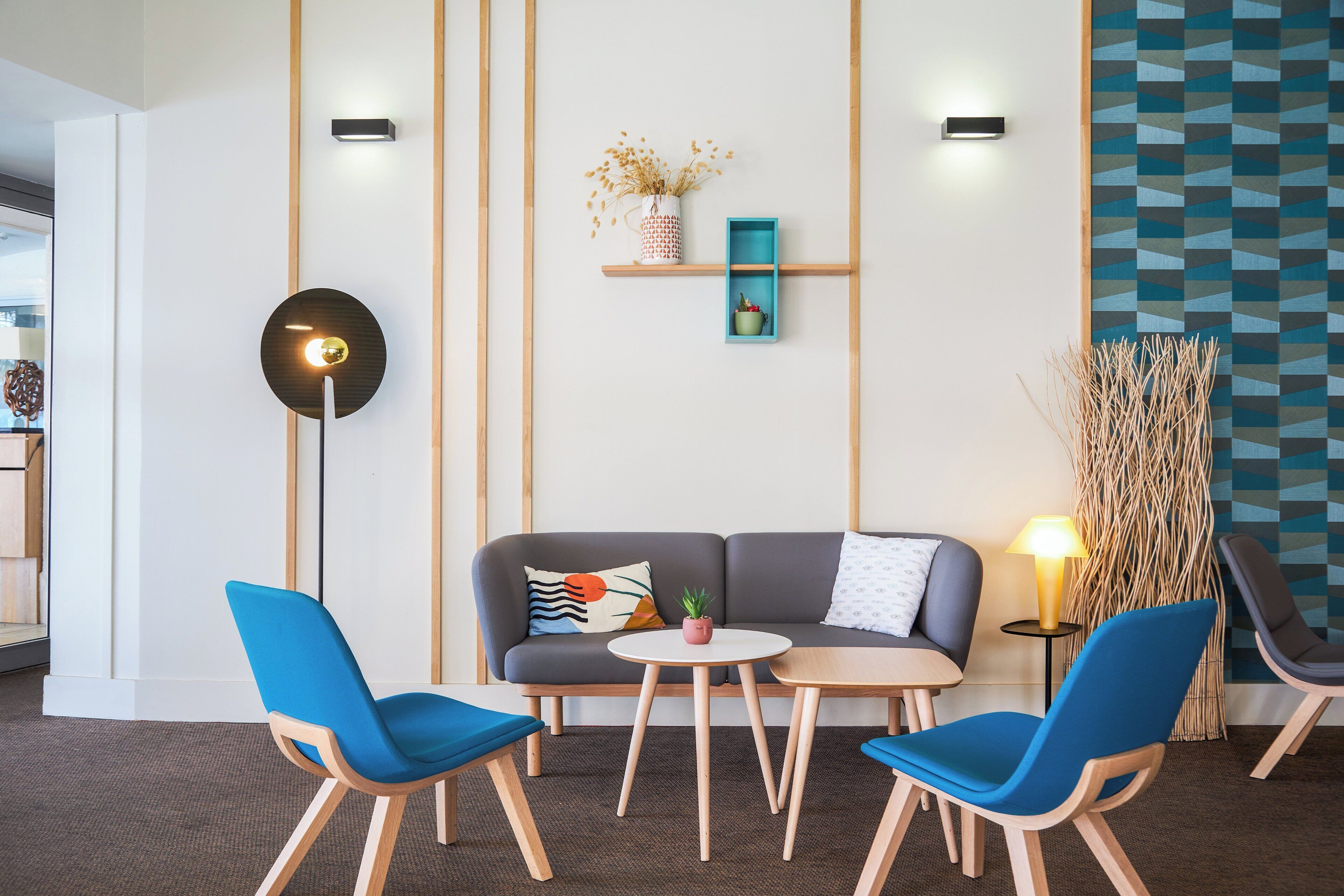 Una moderna zona relax con un divano, due poltrone blu, un tavolino e una lampada da terra.