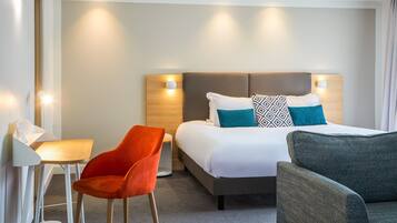 Une chambre d’hôtel avec un lit, deux chaises, un bureau et une table de chevet.
