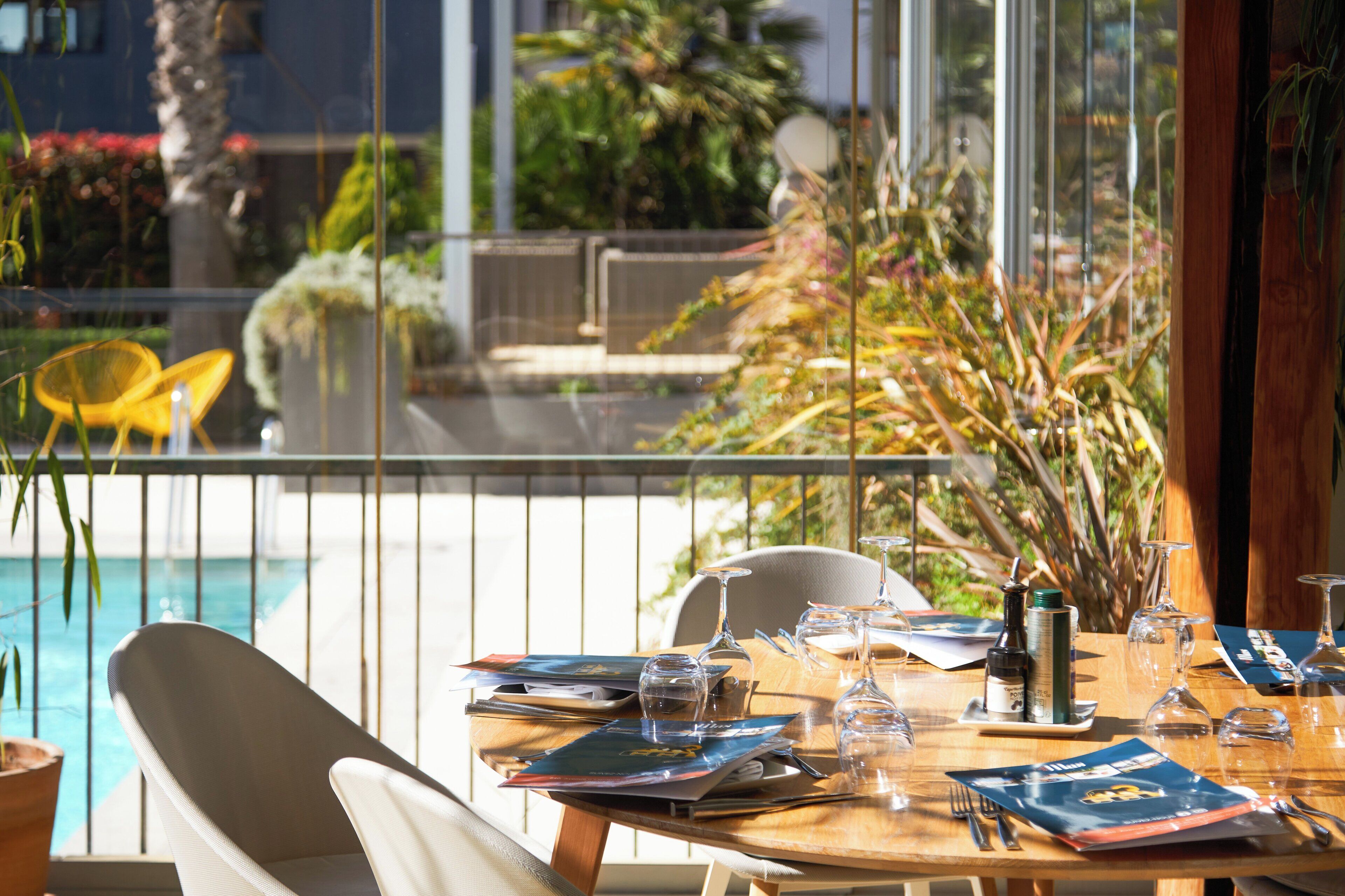 A dining table set with glassware, a menu, and a bottle of wine, overlooking a pool and garden.