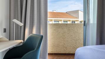Habitación de hotel con cama, escritorio, silla y vista a edificios a través de una ventana.