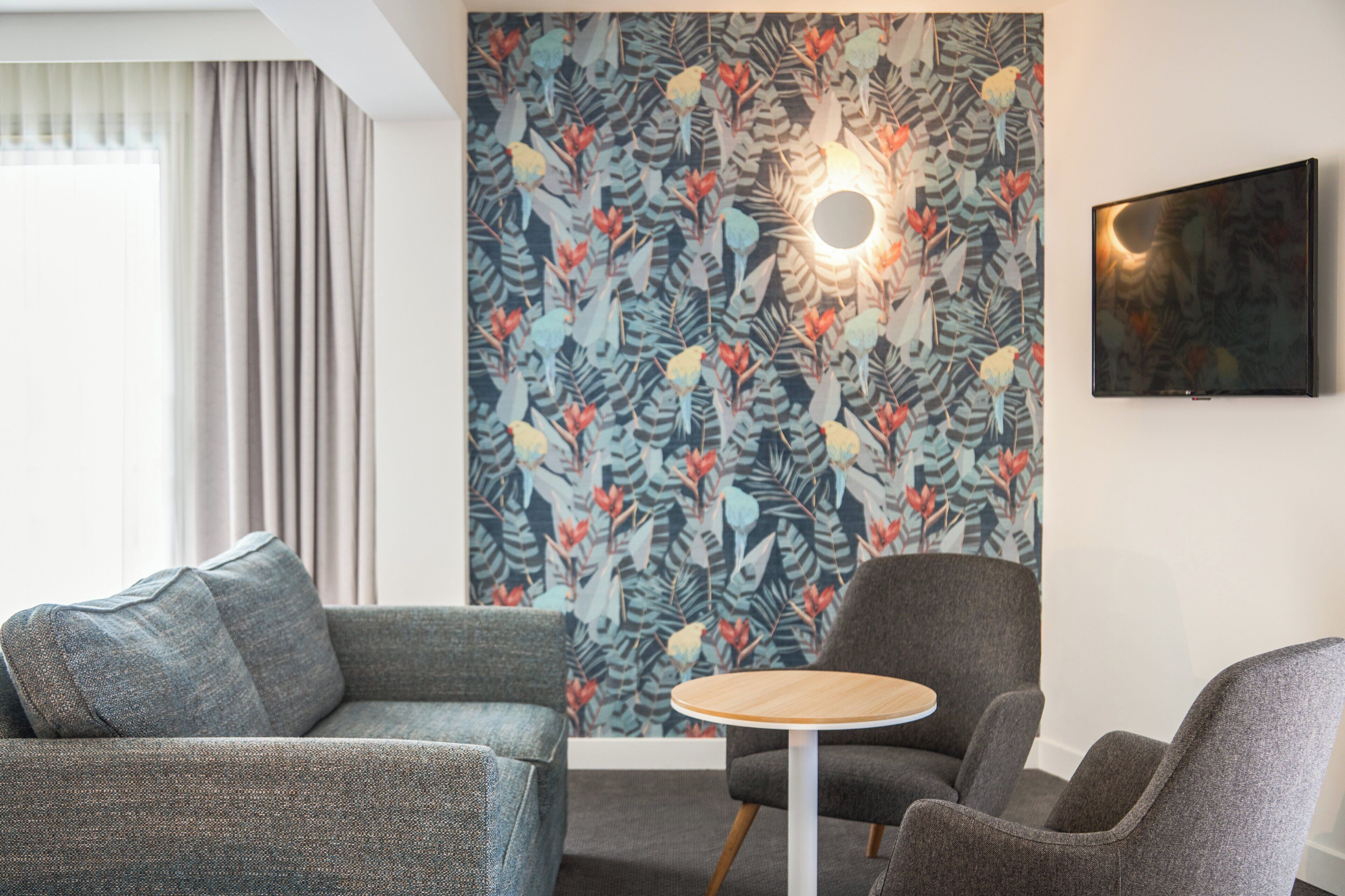 Una sala de estar moderna con papel tapiz estampado, una mesa redonda de madera y dos sillones grises.