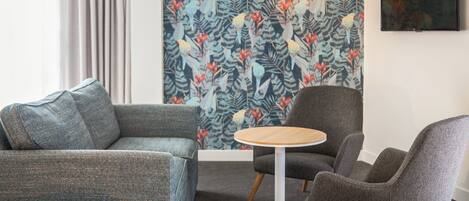 Una sala de estar moderna con papel tapiz estampado, una mesa redonda de madera y dos sillones grises.