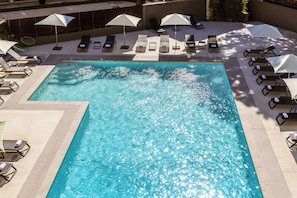 Una piscina rectangular con agua cristalina y azul, rodeada de sillones de playa y sombrillas.