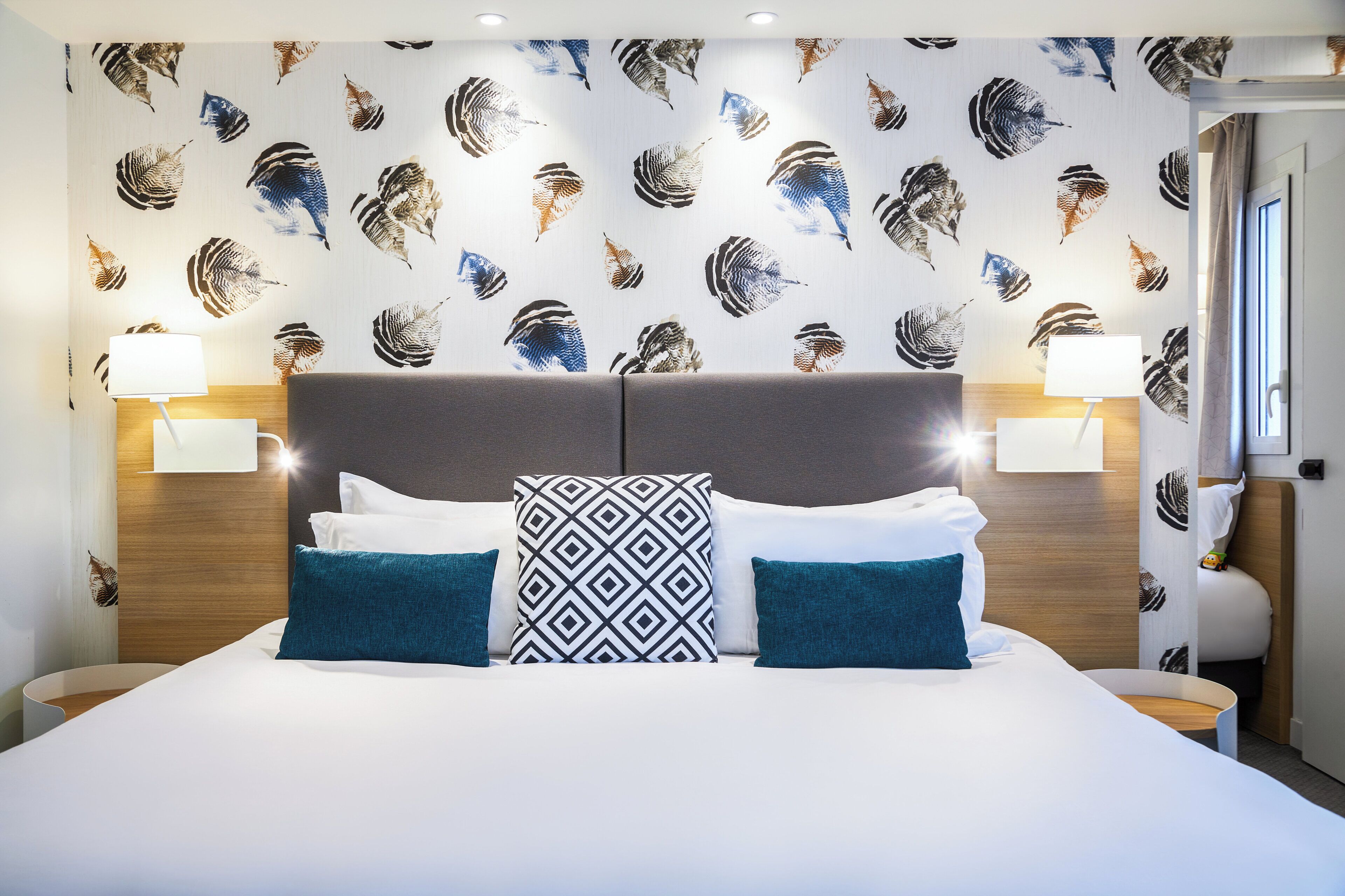 Habitación de hotel con una cama grande, dos mesitas de noche y una pared con un diseño de hojas.