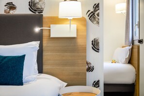 A hotel room with a bed, a bedside table, a lamp, and a wall-mounted light fixture.
