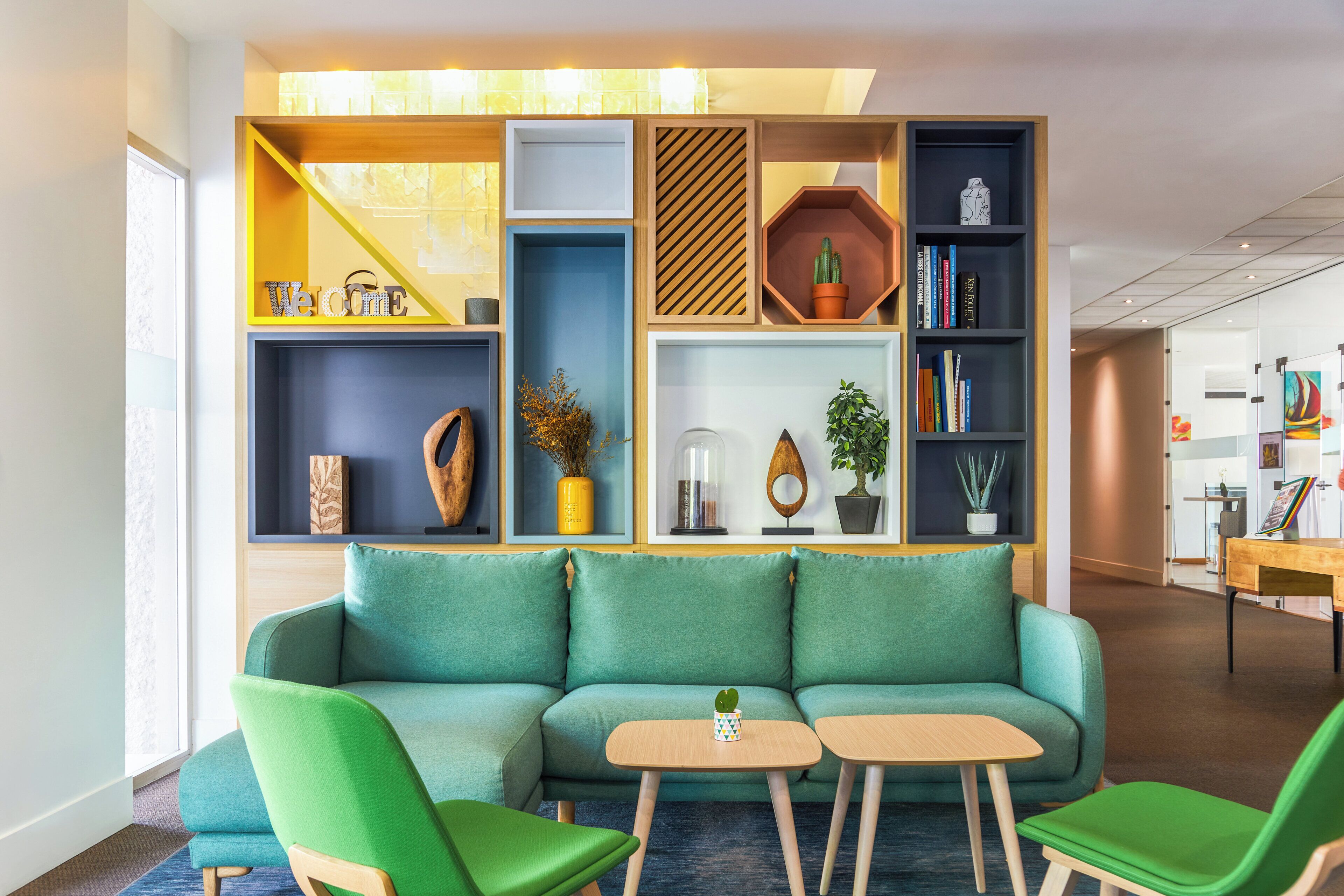 A modern living room with a green sofa, two matching armchairs, a coffee table, and a bookshelf filled with books and decorative items.
